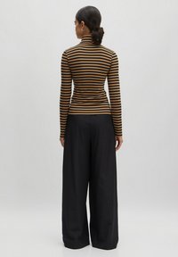 Gestreepte coltrui in bruin en zwart stof, strak ontwerp met lange mouwen; gecombineerd met losse zwarte wijde broek.