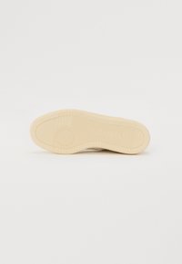 Skolet i off-white gummi med en teksturert overflate, som har horisontale og vertikale riller, samt et sirkulært preg nær hælen.