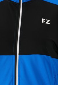 Jacka med dragkedja som har en färgblockdesign med svarta, blå och vita inslag. Materialet är slätt med kontrasterande sömmar och en "FZ"-logotyp.