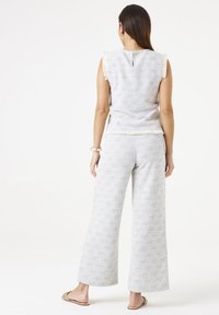 Ensemble deux pièces texturé bleu clair et blanc avec un haut sans manches et un pantalon à jambe large, présentant des bords effilochés et une coupe décontractée.