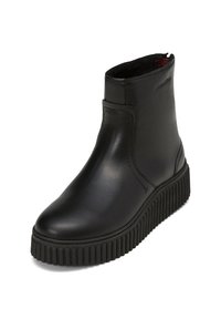 Bottine en cuir noir avec semelle épaisse à relief, bout rond, fermeture éclair latérale et logo embossé discret près du bord supérieur.