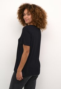 Sort kortærmet t-shirt med en afslappet pasform, blødt stof, rund halsudskæring og slidser i siden, kombineret med mørke jeans.