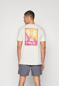 Krämfärgad bomulls-T-shirt med en stor flerfärgad grafik på baksidan som har en triangulär bergsdesign och texten "TRAIL" längst ner.
