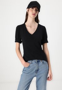 Sort, tætsiddende top med puffærmer og V-hals, parret med lyseblå jeans. Stoffet ser glat ud med fine syninger.