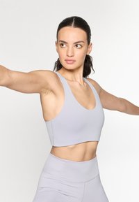 Sujeción deportiva gris claro con escote redondeado, tirantes anchos y diseño corto. Textura suave y costuras mínimas para mayor comodidad.