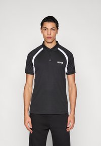 Μαύρο πόλο μπλουζάκι με λευκές λεπτομέρειες και λογότυπο στο αριστερό στήθος. Μανίκια κοντά και πατιλέτα με κουμπιά. Λεία υφή, αθλητική εφαρμογή.