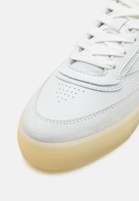 Baskets gris clair avec une tige en cuir lisse, des accents en daim doux, des perforations sur le bout et une semelle en gomme translucide.