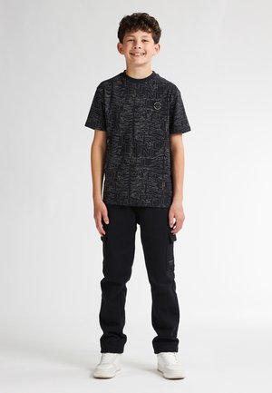 Zwarte graphic T-shirt met abstracte ontwerpen, gecombineerd met zwarte cargo-broeken. Witte sneakers maken de outfit compleet. Glad stoftextuur.
