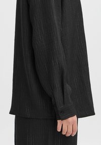 Zwart gestreepte blouse met lange mouwen, gemaakt van lichtgewicht stof. Heeft een knoopmanschette en een subtiele glans met verticale streepjes.