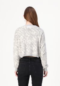 Kuttet lysegrå genser med teksturert bølget mønster, strikket stoff og ribbede mansjetter. Båret med høytlivde svarte jeans.