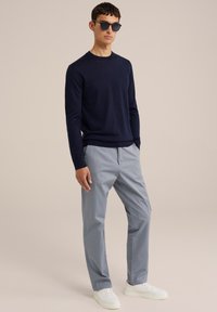 Námořnický svetřík s kulatým výstřihem, světle modré chinos kalhoty a bílé tenisky. Model nosí kulaté černé sluneční brýle. Hladká textura, ležérní střih a čisté linie.