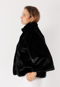 Giacca di pelliccia sintetica nera con colletto alto, maniche ampie e una texture morbida. Presenta una vestibilità comoda e una finitura liscia.