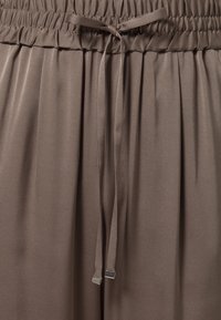 Elastyczny pas z wiązanym sznurkiem na miękkim, gładkim, taupe'owym materiale z subtelnymi plisami poniżej pasa.