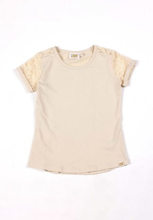 T-shirt beige à manches courtes, avec des manches en dentelle florale transparente et une encolure ronde, sur fond blanc.
