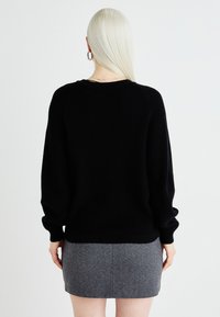 Pulover negru, tricotat cu nervuri, cu umeri lăsați și mâneci pline, asortat cu o fustă mini gri, cu model herringbone. Design simplu și texturat.