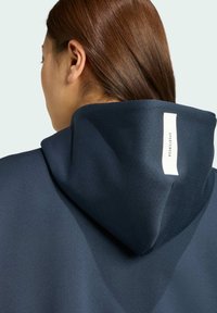 Felpa con cappuccio blu navy realizzata in un tessuto morbido e texturizzato. Un'etichetta bianca sul retro riporta la parola "SPORTWEAR."