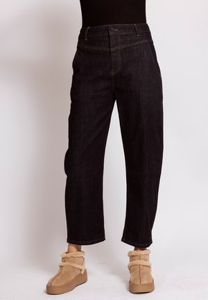 Person wearing high-waist straight black jeans paired with beige furry ankle boots against a plain background.