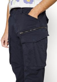 Námořnické cargo kalhoty z měkké, strukturované tkaniny. Obsahují více kapes, včetně boční kapsy na zip pro zvýšenou funkčnost.