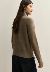 Jersey de cuello alto marrón, de punto, con bajo y puños acanalados. Textura suave; se lleva con jeans de mezclilla oscuros.
