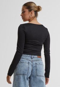 Svart langermet topp med rund hals, tettsittende silhuett og glatt tekstur, kombinert med lyseblå høytlivsjeans med baklommer.