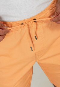 Pantalones cortos naranjas con cintura elástica y cordón ajustable, que presentan terminales de metal. Tejido suave y ligero con un diseño liso.