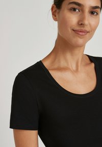 T-shirt nera a maniche corte con scollo a U, realizzata in tessuto morbido. Presenta cuciture curate e una silhouette aderente, senza motivi particolari.