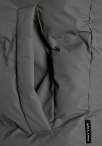 Gray puffer jacket detail featuring a textured fabric, a large side pocket, and a small label tag reading "JACK & JONES."