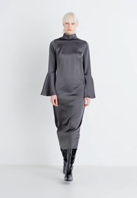 Lang, slim-fit kjole i mørkegrå satinmateriale med høy krage og klokkeermaler, som har et gulvlangt design og er kombinert med knærhøye støvler.