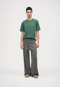 Πράσινο βαμβακερό μπλουζάκι με κοντά μανίκια και στρογγυλή λαιμόκοψη, σε συνδυασμό με σιέλ τζιν παντελόνι φαρδιάς γραμμής. Μπεζ υποδήματα ολοκληρώνουν την εμφάνιση.