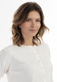 Fehér kötött kardigán kerek nyakkivágással és diszkrét gombos záródással, puha textúrával és testhezálló vonalakkal.