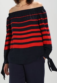 Top off-shoulder con ampia scollatura elastica, caratterizzato da audaci righe orizzontali rosse e blu navy, tessuto testurizzato e dettagli con maniche legate.