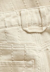 Κοντινή λήψη υφάσματος εκρού με υφή, σχέδιο πλέγματος με ραφές, θηλιές ζώνης και γωνία τσέπης σε ρούχο.