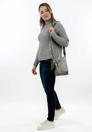 Grey knitted sweater, dark blue jeans, and light sneakers. The metallic grey handbag features a front zip pocket and a tassel detail.
