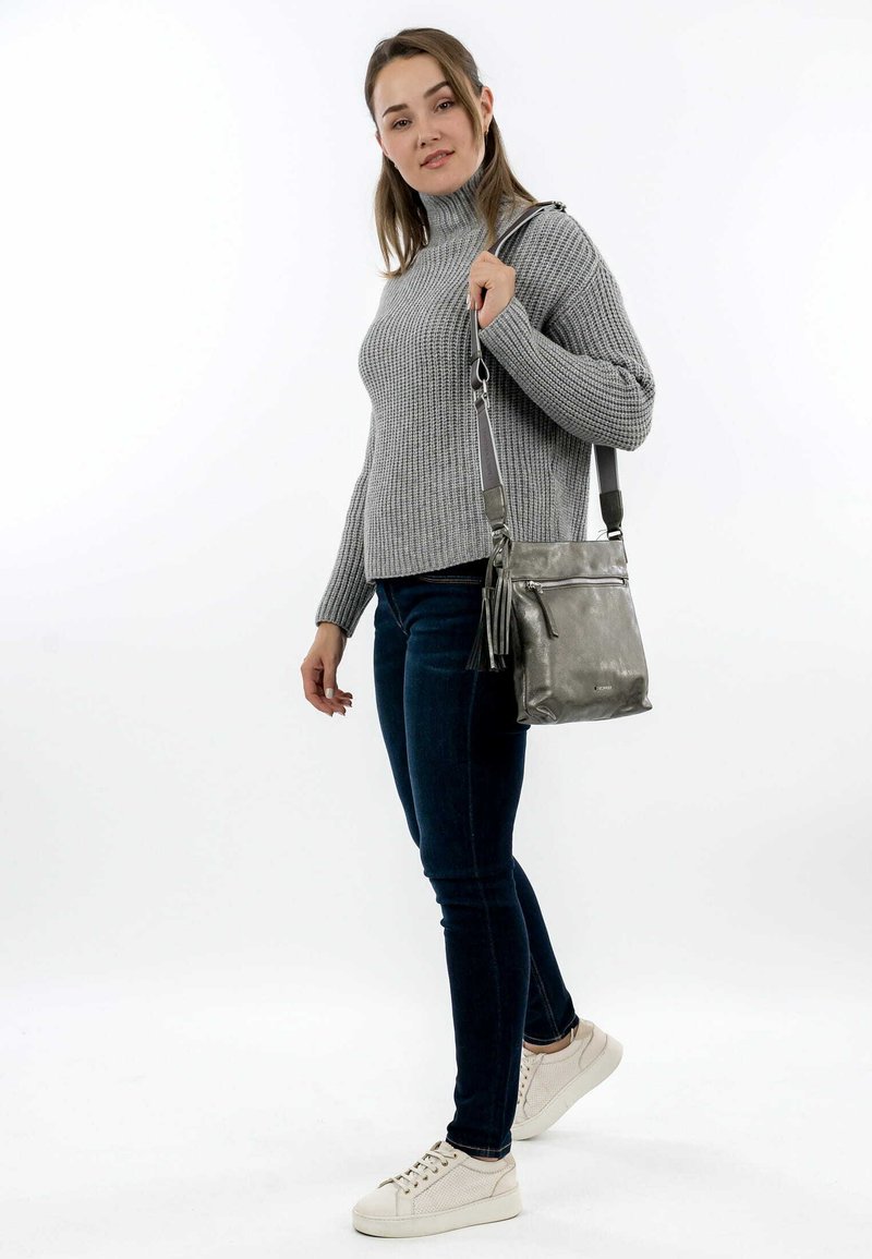 Grey knitted sweater, dark blue jeans, and light sneakers. The metallic grey handbag features a front zip pocket and a tassel detail.