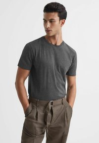 T-shirt gri cu mânecă scurtă, dintr-un material moale, completat de pantaloni maro plisati cu o curea, având buzunare laterale și o croială lejeră.