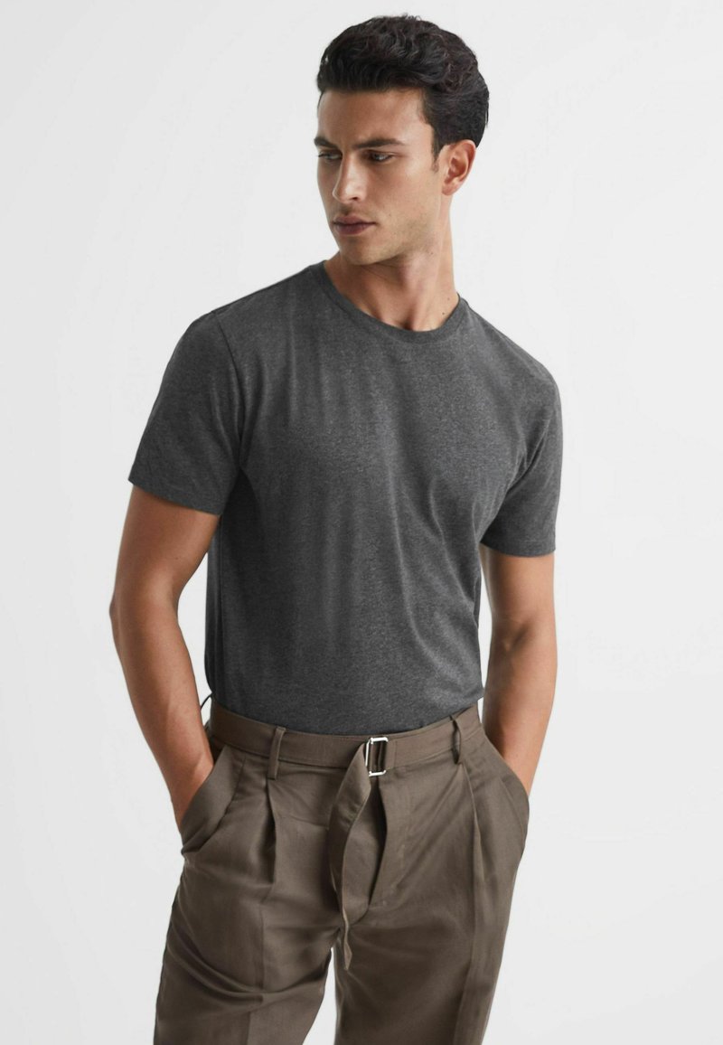 T-shirt gri cu mânecă scurtă, dintr-un material moale, completat de pantaloni maro plisati cu o curea, având buzunare laterale și o croială lejeră.