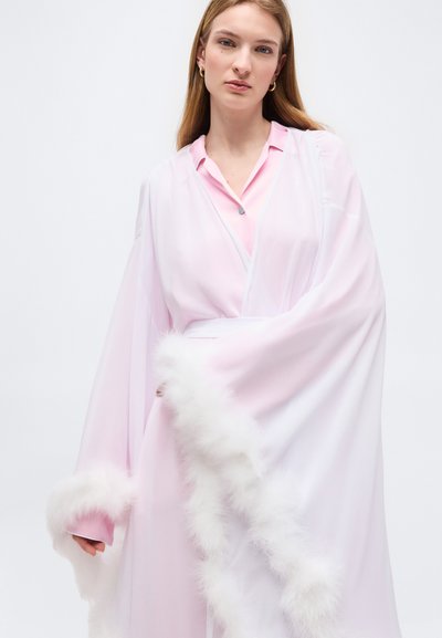 Γυναίκα με ίσια ξανθά μαλλιά, που φοράει ροζ σατέν ρόμπα και διαφανές λευκό σάλι με αφράτο λευκό περίγραμμα, σε απλό λευκό φόντο.