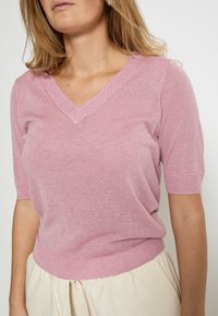 Top rosa a maniche corte in maglia con scollo a V, caratterizzato da una finitura leggermente strutturata e orlo a coste, che valorizza una vestibilità ampia.