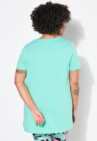 Mentos grøn kortærmet T-shirt med rund hals, glat tekstur og afslappet pasform, parret med mønstrede yoga-bukser. Bagview vist.