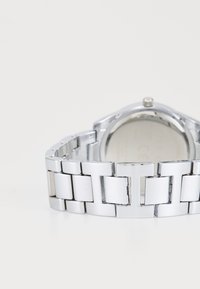 Montre en métal argenté avec un bracelet à maillons poli, comprenant des maillons rectangulaires et un boîtier rond métallique avec un fond uni.