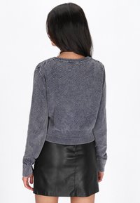 Pulover texturat de culoare navy, cu guler și mansete ribbate. Are un tiv ajustat și manșon lung, asociat cu o fustă mini din piele neagră.