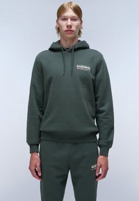 Groene hoodie met trekkoord, ribgebreide manchetten en zoom. Bevat een logo-opdruk op de borst. Gecombineerd met bijpassende joggerbroeken, ook in het groen.