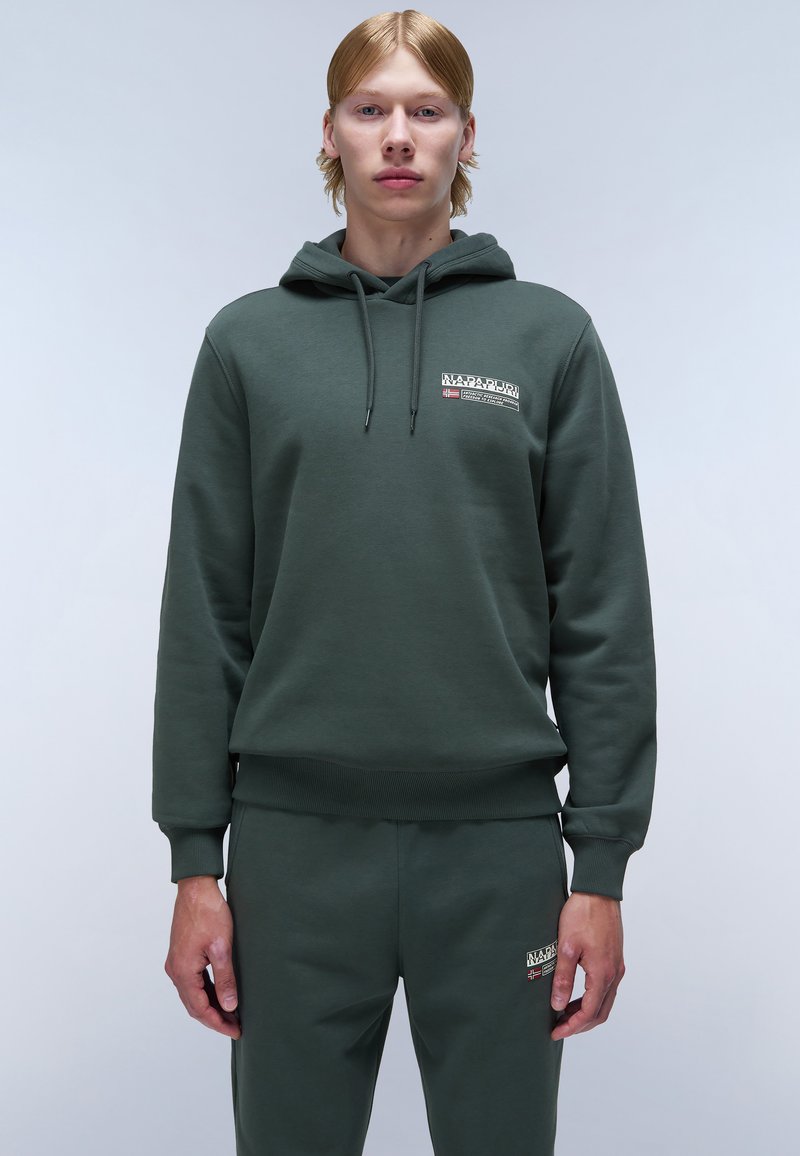 Groene hoodie met trekkoord, ribgebreide manchetten en zoom. Bevat een logo-opdruk op de borst. Gecombineerd met bijpassende joggerbroeken, ook in het groen.
