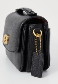 Schwarze Lederhandtasche mit strukturiertem Finish, goldenen Beschlägen und einem angehängten Schlüsselanhänger. Verfügt über einen Klappenverschluss und eine kompakte rechteckige Form.