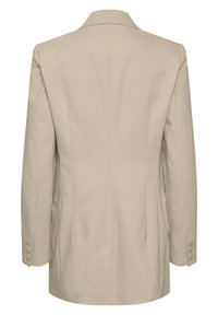 Blazer beige con una textura suave, que presenta un pico y cuatro botones en cada puño. La parte posterior tiene un detalle de costuras verticales.