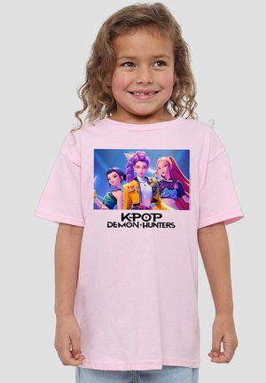 Light pink cotton t-shirt featuring a central graphic of three characters with the text "KPOP DEMON HUNTERS" below. Short sleeves, relaxed fit.