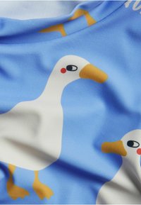 Sininen kangas, jossa on toistuva kuvio vaaleansinisen taustan päällä olevista sarjakuvamaisista valkoisista ankoista, joilla on oranssit nokat ja keltaiset jalat.