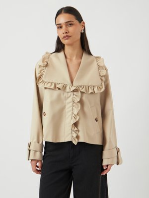 Beige cropped jacket with a large frilled collar, textured fabric, button closures, and cuff details, paired with dark pants.