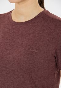 Maroon idrottströja i lätt, strukturerad tyg. Har en rund halsringning och en subtil "ENDURANCE"-logotyp på bröstet.