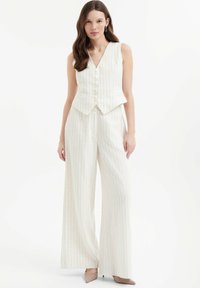 Beige, gestreepte tweedelige outfit met een mouwloze V-hals vest met knopen en brede broekspijpen gemaakt van een gestructureerde, lichte stof.